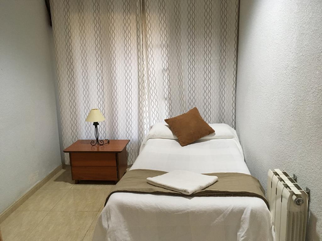 Habitación con una cama individual, mesilla de madera, lámpara y radiador.