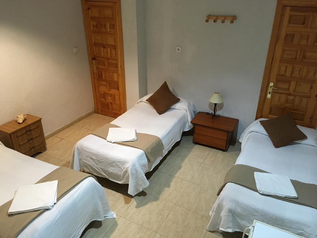 Habitación con varias camas individuales, mesillas y puertas de madera.