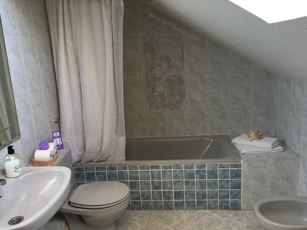 Baño con bañera, lavabo, inodoro y bidé bajo un techo inclinado.