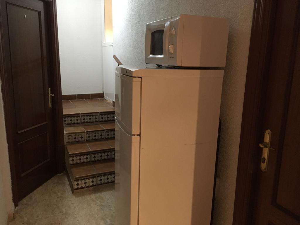 Zona común junto a una escalera, con nevera y microondas.